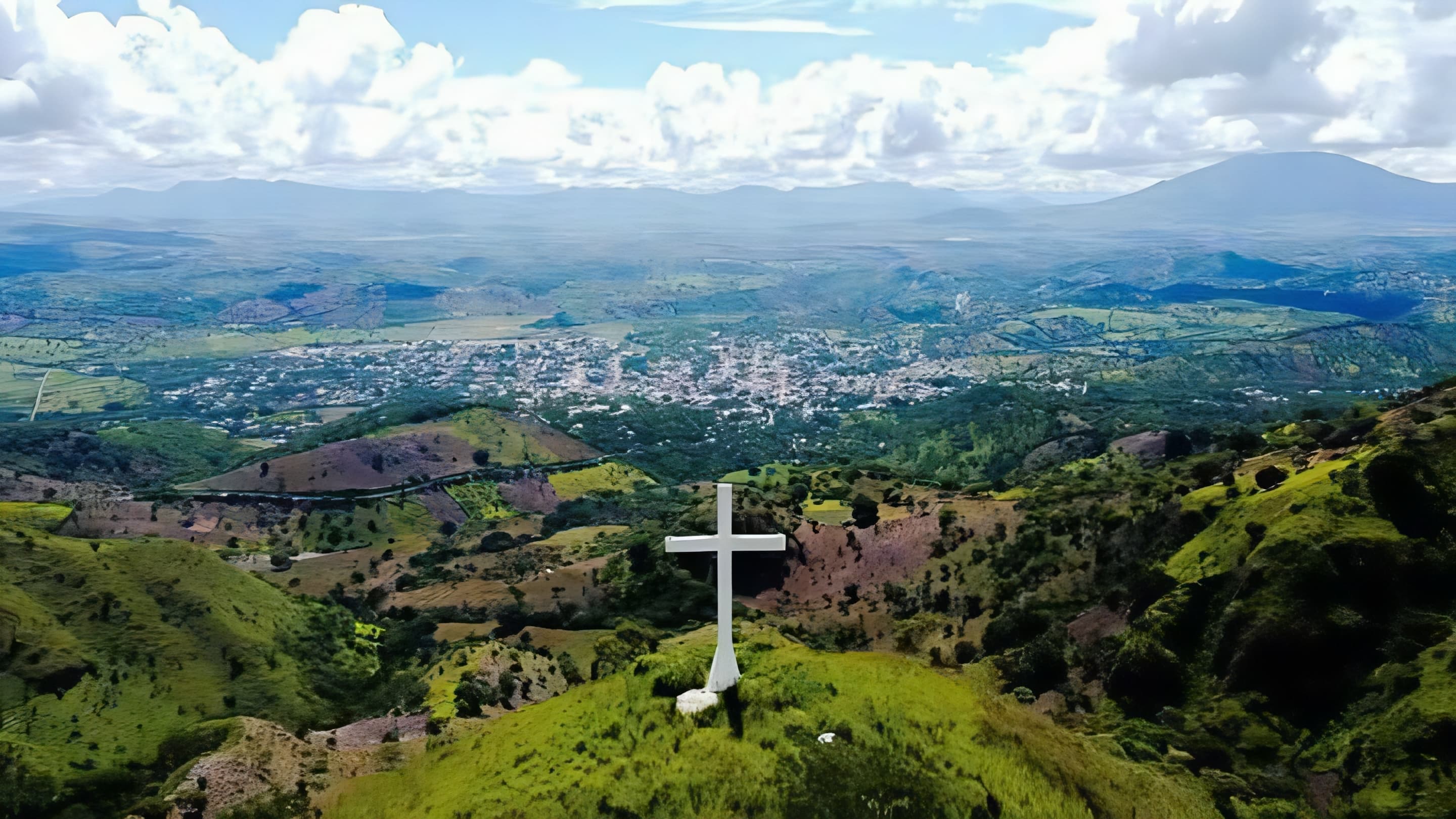 Vista aérea del valle de San Luis Jilotepeque con una cruz blanca en la cima de un cerro
